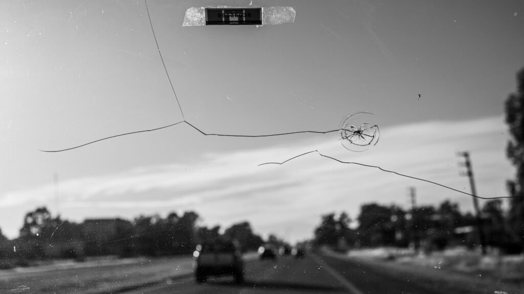 Black and white shot of a cracked windshield, driving on a Buenos Aires road.